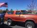 1979 Ford Bronco - An orange Ford Bronco is parked under a bright blue sky with an American flag waving in the background.