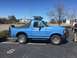 1979 Ford Bronco - A blue Ford Bronco is parked in a lot under a clear sky, showing its side profile and front end.