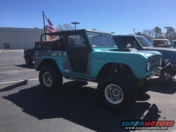 Teal Ford Bronco with an American flag on a pole, parked next to another vehicle