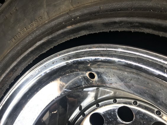 Close-up of a damaged tire bead and chrome rim with a valve stem hole