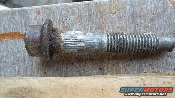 Rusted lug bolt with a flanged head and splined shaft, lying on a wooden surface