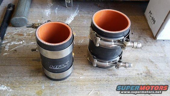 Two black silicone hoses with orange interiors and metal clamps on a wooden surface. One hose has "HPS" logo