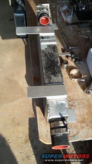 Intercooler with red-lined hoses and aluminum mounting brackets on a workbench