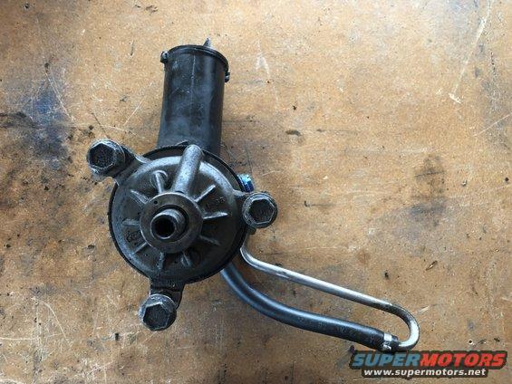 power steering pump with hoses attached, resting on a wooden surface