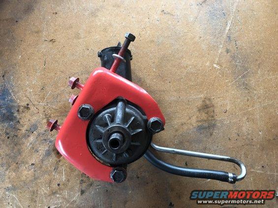 Red power steering pump with black hose and metal mounting bolts on a wooden surface
