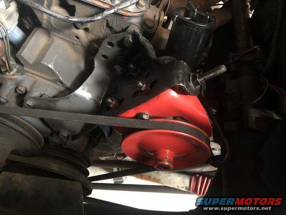 Close-up of a red and black engine motor mount bracket with a belt and pulley