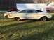 1960 Ford Starliner - A white 1960 Ford Starliner coupe sits in a grassy field, showing extensive damage to its rear passenger side.