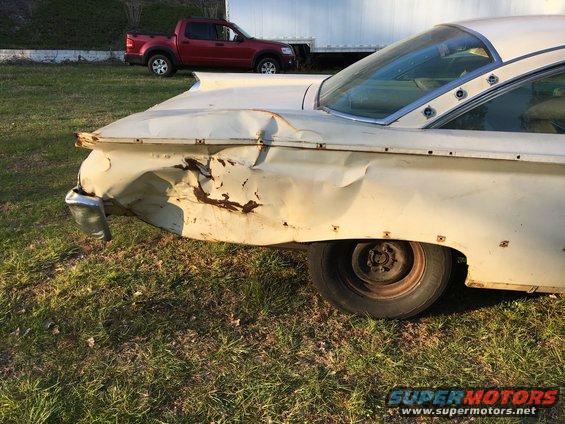 Damaged white 1959 car rear quarter panel with chrome bumper