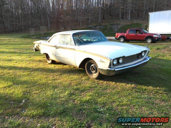 1960 Ford Starliner parked on grass with a red Ford Explorer and a white trailer in the background