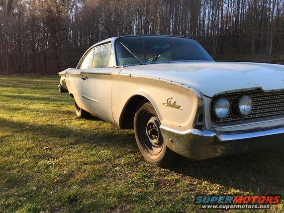 White 1960 Ford Starliner coupe parked on grass, front quarter view, showing chrome bumper and Starliner badging