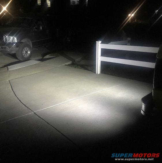 Black truck front view at night, headlights on, parked on concrete driveway