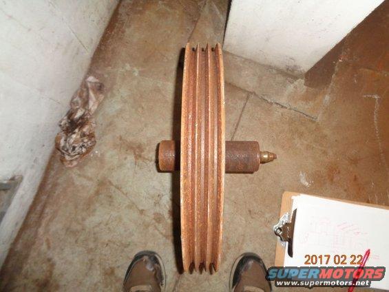 Rusty multi-groove pulley with a shaft, resting on a concrete floor