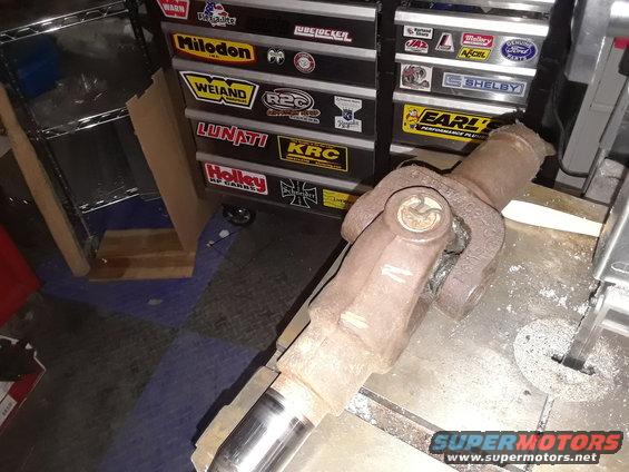 Driveshaft U-joint with rust and wear, resting on a metal surface near a band saw