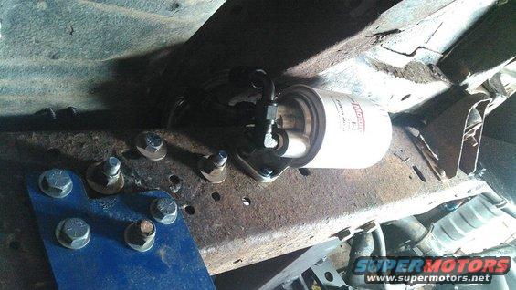 Motorcraft fuel filter mounted to rusty vehicle frame with bolts and blue bracket