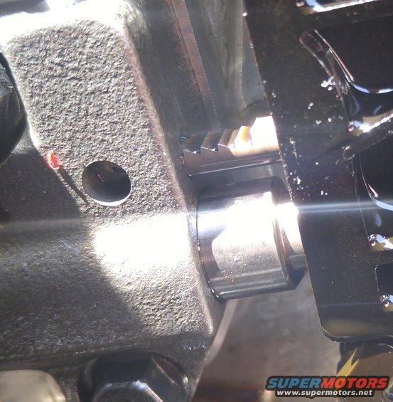 Close-up of a metal gear with teeth meshing with a shaft, likely inside an engine