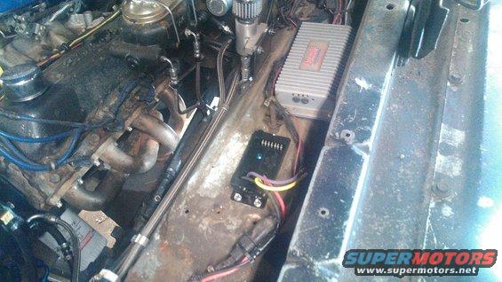 Engine bay with a V8 engine, headers, and aftermarket amplifier and control box