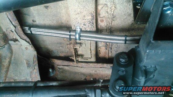 Underside of a vehicle showing braided hoses secured with zip ties to rusty metal frame components