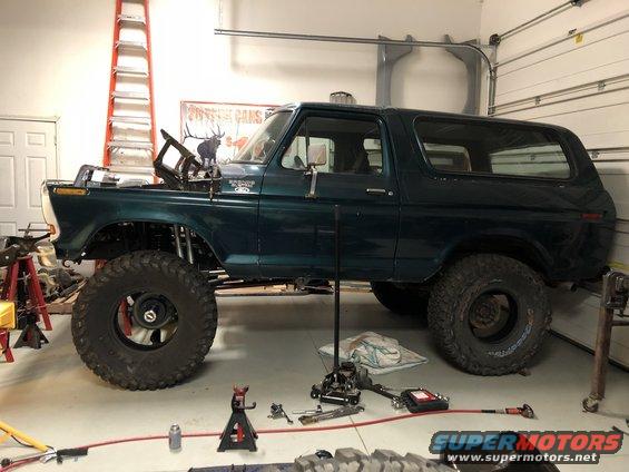Green Ford Bronco with lifted suspension and large tires, hood open, in a garage with tools around it