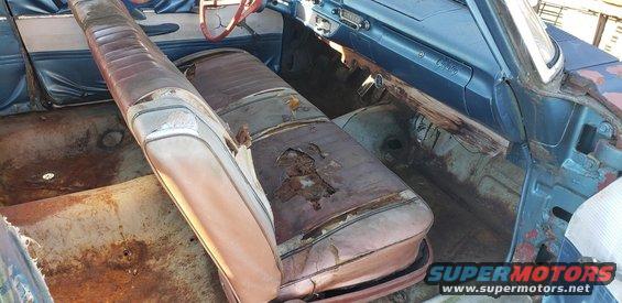 Interior of a 1962 Ford Galaxie with torn brown seats, blue dashboard, and rusted floor panels