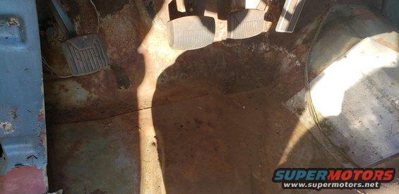 Interior floor pan of a vehicle showing rusted metal and brake and accelerator pedals