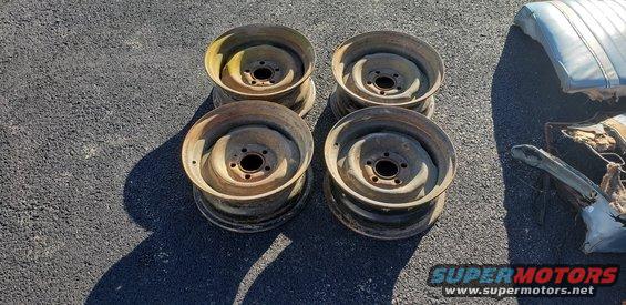 Four rusty steel wheels and torn car seat cushions on asphalt