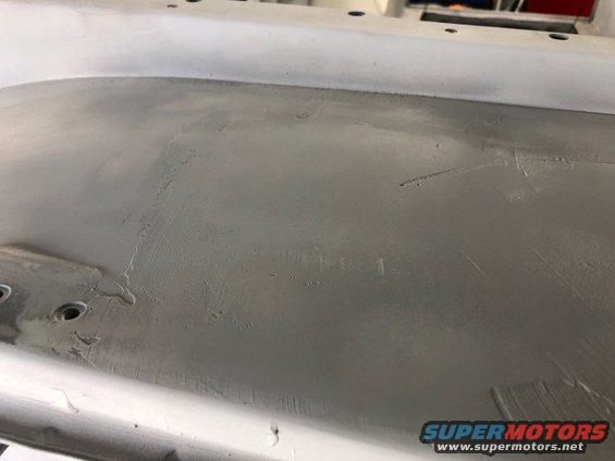 Primed car body panel with visible sanding marks and some small holes