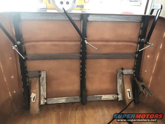 Vehicle bed interior with custom metal bracing and brown fiberglass lining. Visible measurements on metal brackets