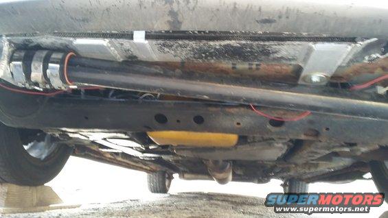 Underside view of a car, showing the exhaust system, frame, and some wiring