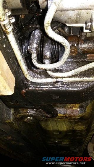 Underside view of a greasy power steering rack and pinion with hoses attached
