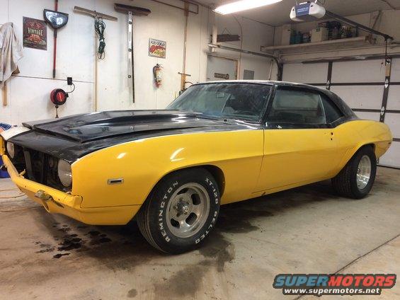 1969 Chevrolet Camaro with yellow body and black hood, parked in a garage