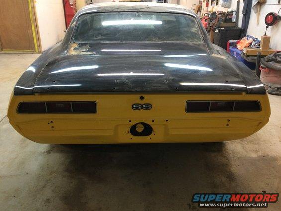 Yellow 1969 Chevrolet Camaro SS rear view, in a workshop, with black primer on the trunk and roof