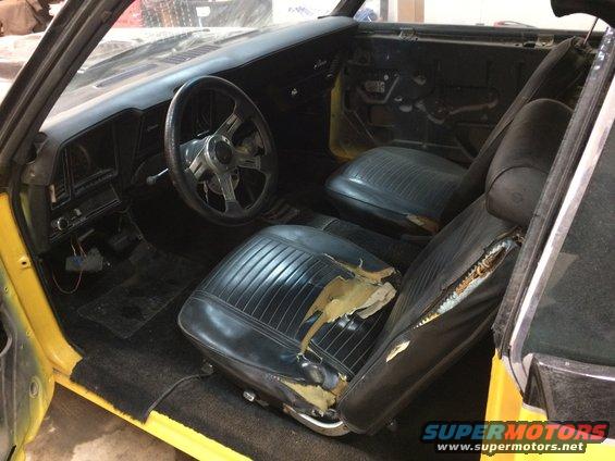 Yellow 1969 Chevrolet Camaro interior with torn black vinyl seats and aftermarket steering wheel