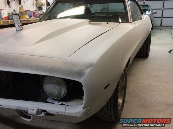 1969 Chevrolet Camaro body in primer, front quarter view, showing primer hood and fender, with a spray can on the hood
