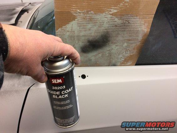 Hand holding SEM 38203 Guide Coat Black spray can near a white car door panel