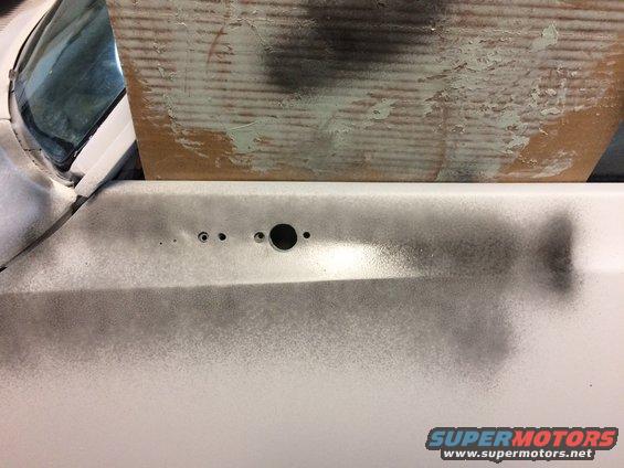 Close-up of a car door panel with holes for a handle and lock. Cardboard is taped over the window area