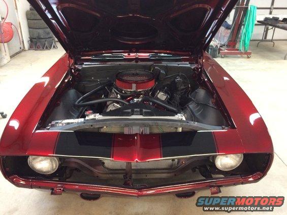 Front view of a red 1969 Chevrolet Camaro with black racing stripes and the hood open, showing the engine