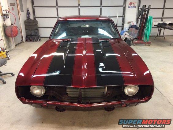 Red 1969 Chevrolet Camaro with black racing stripes, front view, in a garage