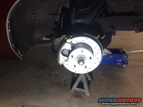 Close-up of a car's front brake rotor and caliper assembly, supported by a jack stand
