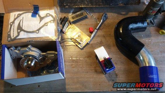 New water pump, gasket set, and intake pipe with tools on a workbench
