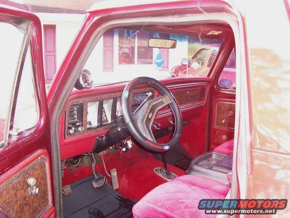 Red 1979 Ford Bronco interior with plush pink seats, wood-grain trim, and a black steering wheel