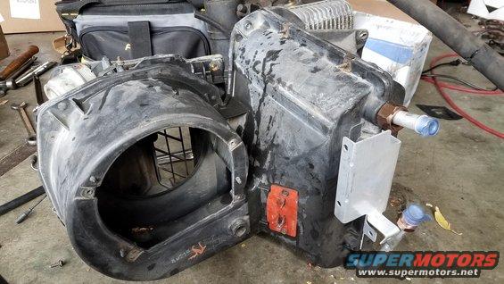 AC evaporator case with fan shroud and some hoses attached, sitting on a garage floor