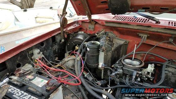 Engine bay with carburetor, battery, and wiring visible