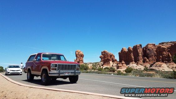 Red and tan Ford Bronco driving on a road with red rock formations in the background