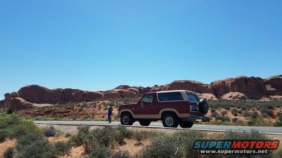 Maroon and tan Ford Bronco parked on a road with red rock formations in the background