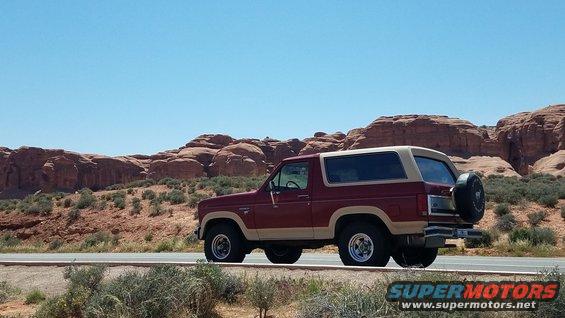 Red and tan 1985 Ford Bronco parked on roadside with desert landscape