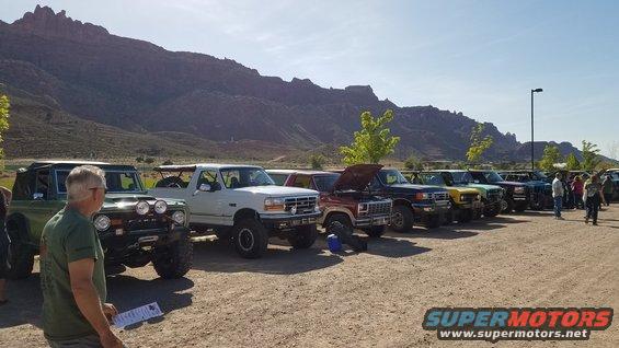 Line of Ford Broncos and trucks, one green, one white, one red with hood up