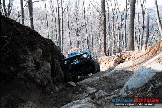 1976 Ford Bronco climbing a difficult rocky trail in a wooded area
