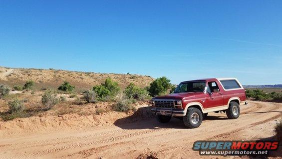 Red 1985 Ford Bronco with white top on dirt road
