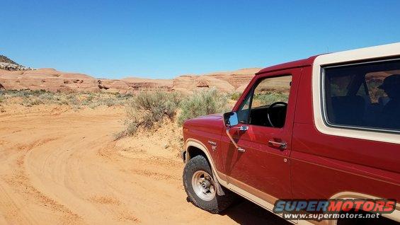 Red Ford Bronco parked on a dirt road with red rock formations in the background