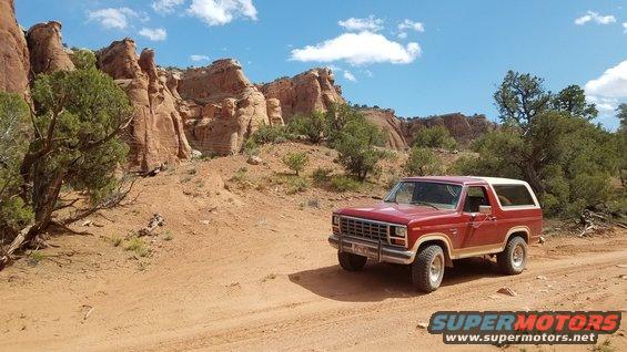 Red Ford Bronco parked on a dirt road in a desert landscape with red rock formations